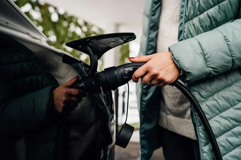 Iemand in een winterjas steekt de laadstekker in een elektrische auto