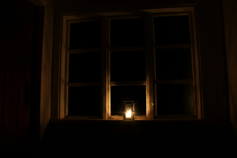 Donkere woonkamer met alleen een kaars bij het raam tijdens een stroomstoring